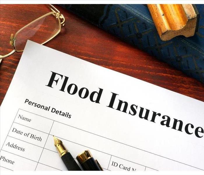 There is a desk with eye glasses a fifty dollar bill and a paper that says "Flood Insurance"
