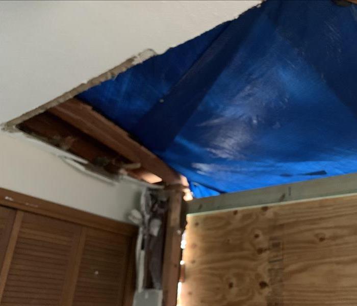 A blue tarp and wood covering holes in a home